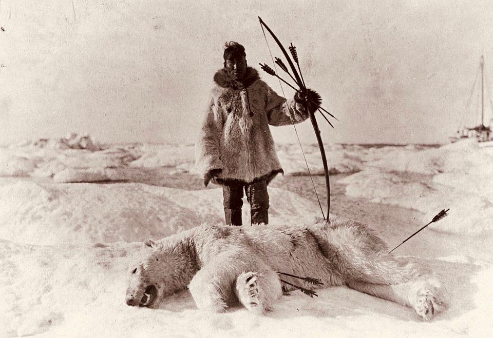 An Inuit hunter stands over a dead polar bear.